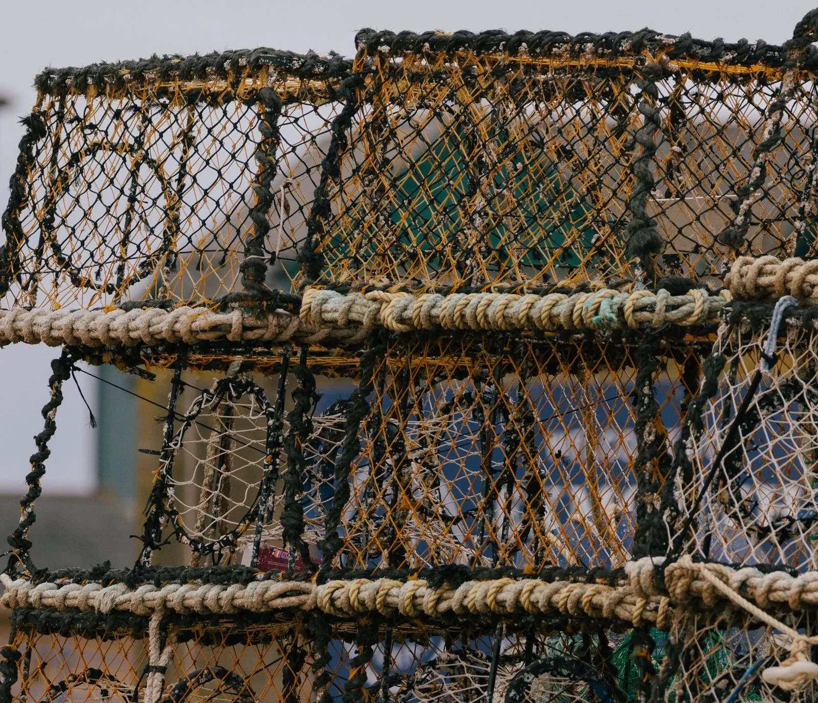 Casiers de pêche empilés sur un quai, filets tressés en mailles serrées jaunes, noires et écrues