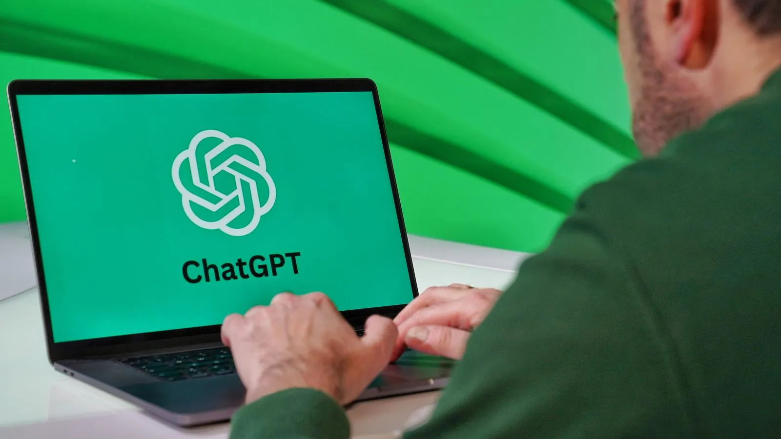 Personne de dos tapant sur un ordinateur portable affichant le logo ChatGPT sur fond vert