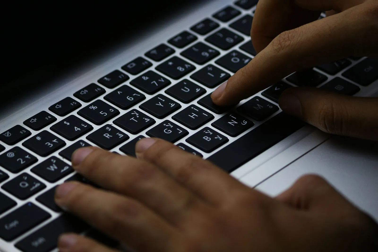 Mains tapant une question sur le clavier d'un ordinateur portable dans la pénombre