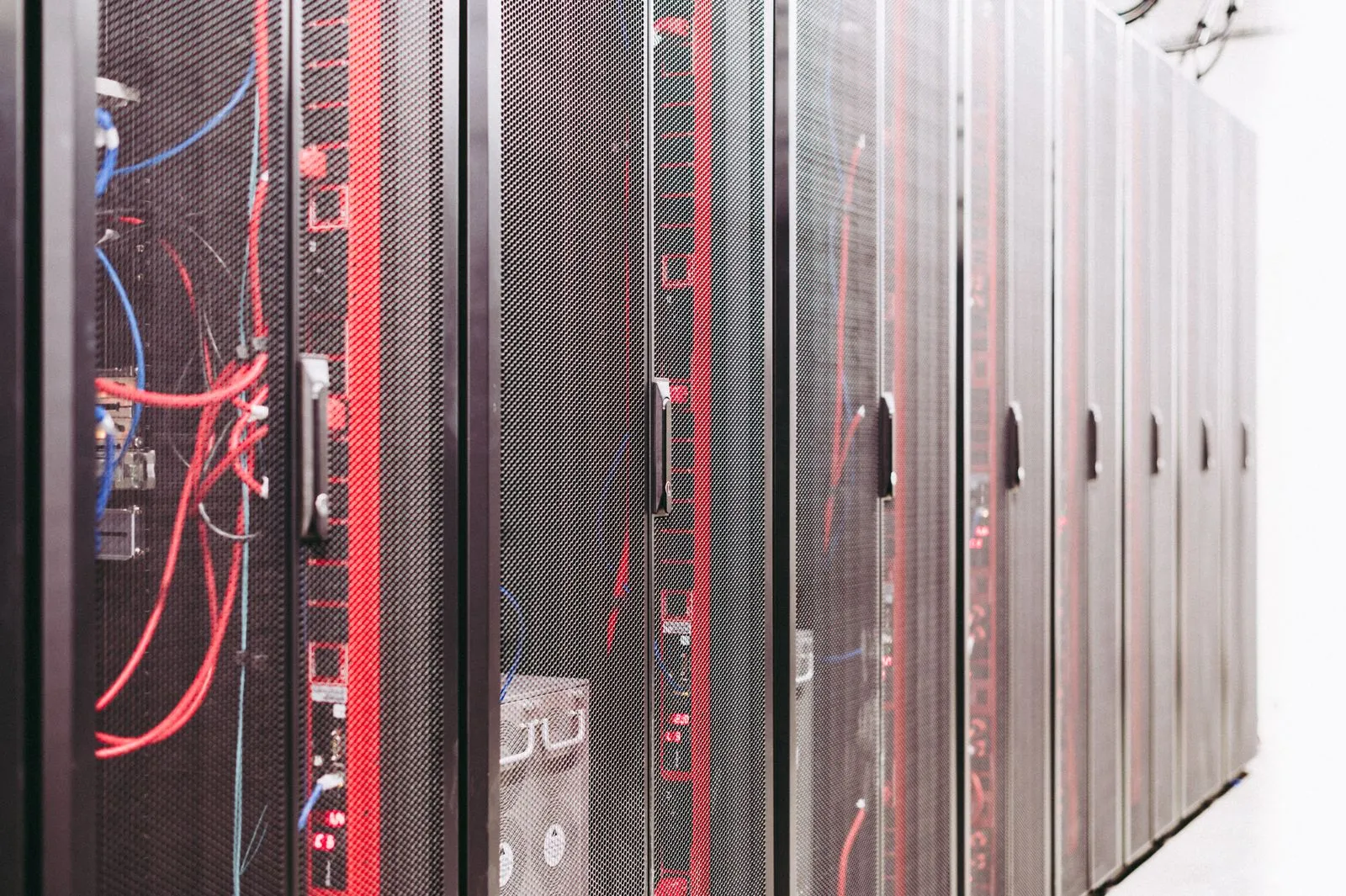Rangée de baies de serveurs dans un datacenter, câbles rouges et bleus visibles à travers les portes grillagées