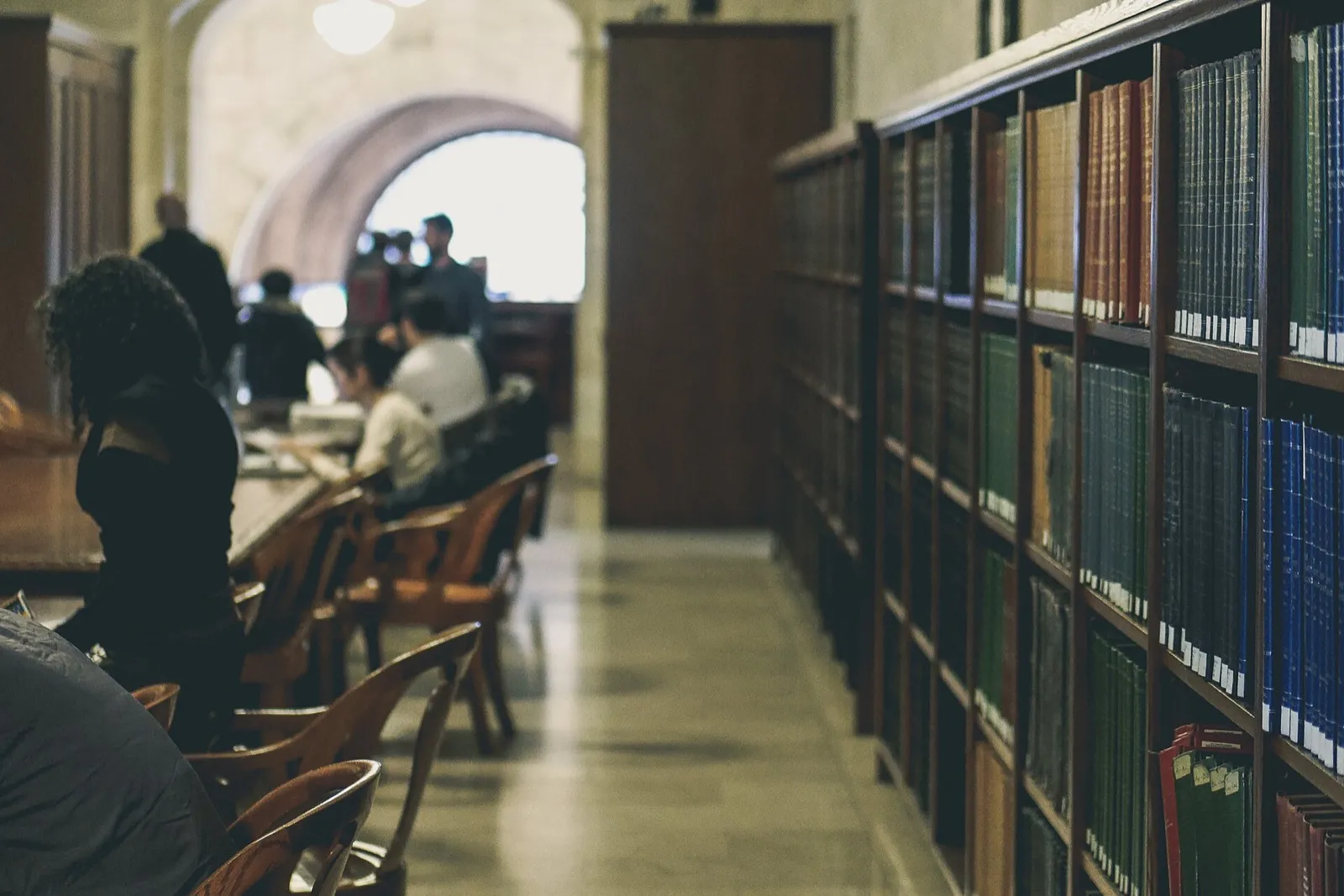 Rayonnages d'une bibliothèque de recherche avec des lecteurs installés à une table de travail